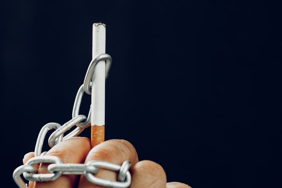 Main enchaînée tenant une cigarette, symbole de l'addiction au tabac et de la dépendance à la nicotine